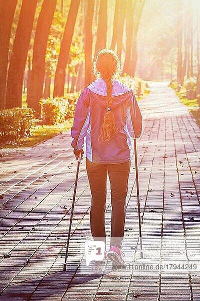 Nordic Walking Abenteuer und Ausübung Konzept  Frau Wandern mit Nordic Walking Stöcke im Park. Mit Lens Flare und Lichtleck