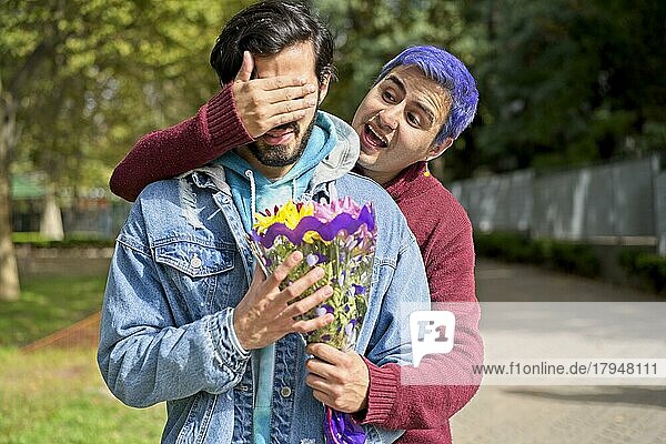 Ein schwules Latino Paar umarmt sich in einem Park  Einer überrascht den anderen mit einem Blumenstrauß als Geschenk