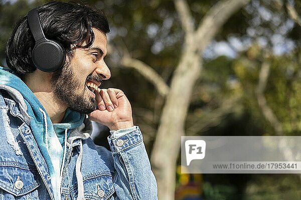 Junger lateinamerikanischer Mann  der im Freien mit Kopfhörern Musik hört. Ausdruck von Glück  gewinnende Haltung