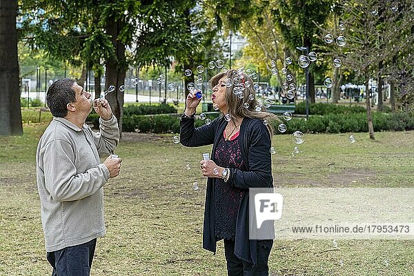 Fröhliches reifes queeres Paar bläst Seifenblasen in einem Park