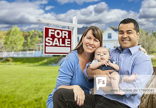 Glückliche junge gemischtrassige Familie vor einem Immobilienschild zum Verkauf und einem neuen Haus
