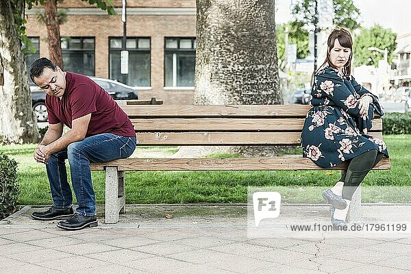 Unglückliches gemischtrassiges Paar  das auf einer Parkbank einander gegenüber sitzt
