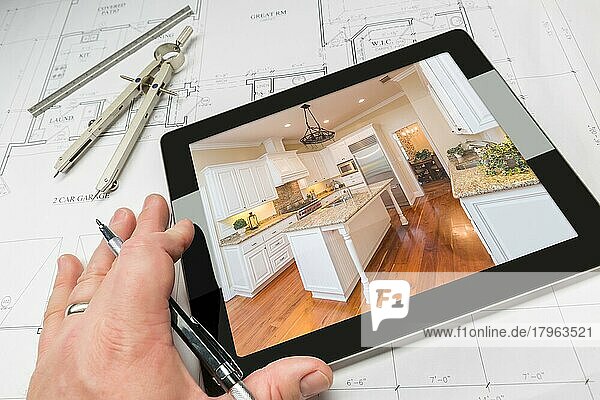 Hand eines Architekten auf einem Computertablett  das ein Foto einer maßgefertigten Küche über Hausplänen  Kompass und Lineal zeigt