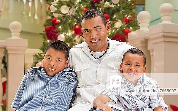 Hispanischer junger Vater und seine Söhne vor dem geschmückten Weihnachtsbaum