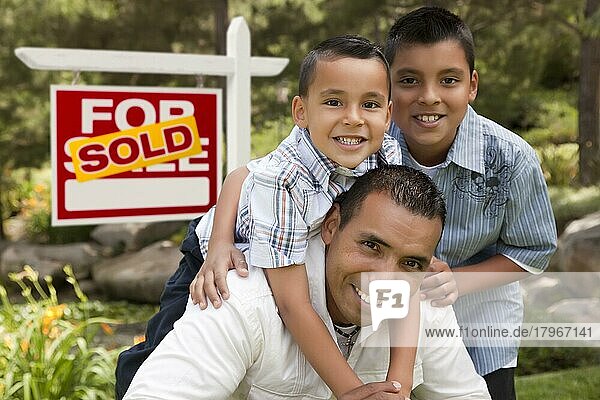 Hispanischer Vater und Söhne vor einem verkauften Haus zum Verkauf Immobilienschild