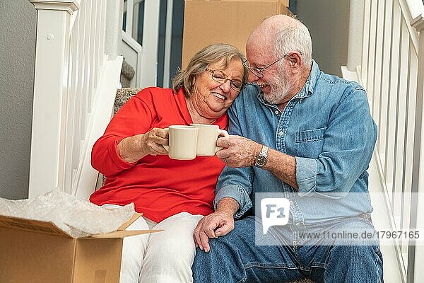 Müdes älteres erwachsenes Paar  das sich mit einer Tasse Kaffee auf der Treppe ausruht  umgeben von Umzugskartons