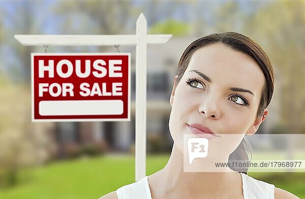 Nachdenkliche hübsche gemischtrassige Frau vor Haus und Haus zu verkaufen Immobilien Schild nach oben und zur Seite schauen