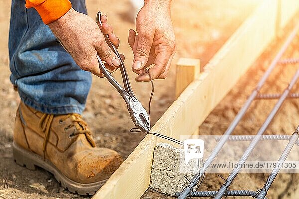 Arbeiter  der mit einer Drahtzange auf der Baustelle Bewehrungsstäbe sichert