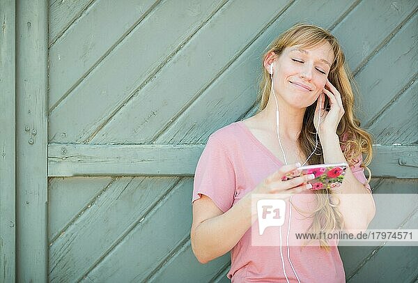 Outdoor-Porträt einer jungen erwachsenen Frau mit braunen Augen  die mit Kopfhörern auf ihrem Smartphone Musik hört