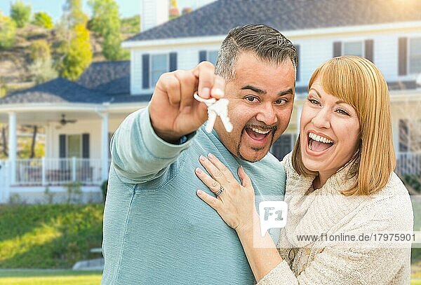 Glückliches gemischtrassiges Paar vor seinem neuen Haus mit Hausschlüssel
