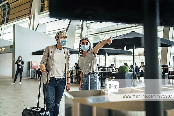 Zwei Reisende mit Schutzmasken diskutieren auf dem Flughafen von Faro mit einer Fluginformationstafel