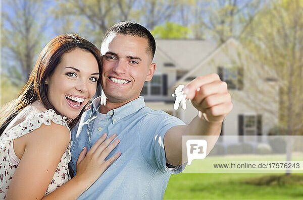 Gemischtrassiges  aufgeregtes Militärpaar vor seinem neuen Haus  das seine Hausschlüssel vorzeigt