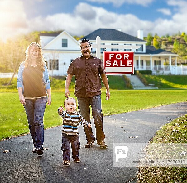 Glückliche gemischtrassige Familie vor einem Haus und einem Immobilienschild zum Verkauf