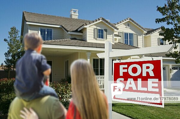 Junge Familie  die sich ein schönes neues Haus mit einem Schild Zu verkaufen ansieht