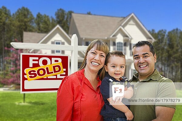 Gemischtrassige junge Familie vor verkauftem Haus  Immobilienschild und neuem Haus