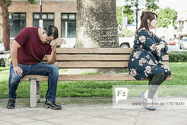 Unglückliches gemischtrassiges Paar  das auf einer Parkbank einander gegenüber sitzt