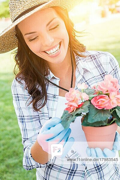 Glückliche junge erwachsene Frau mit Hut und Handschuhen bei der Gartenarbeit im Freien