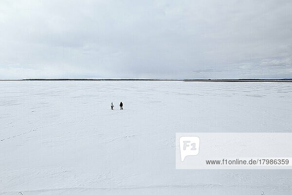 Zwei Menschen stehen auf einer weiten  zugefrorenen Flusslandschaft  Sankt-Lorenz-Strom  Provinz Quebec  Kanada  Nordamerika