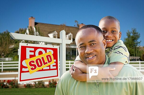 Glücklicher afroamerikanischer Vater und Sohn vor einem neuen Haus und einem verkauften Immobilienschild
