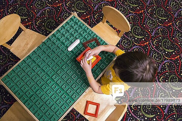 Overhead eines gemischtrassigen Jungen  der an einem Arbeitstisch sitzt und mit Bauklötzen Spielzeug spielt