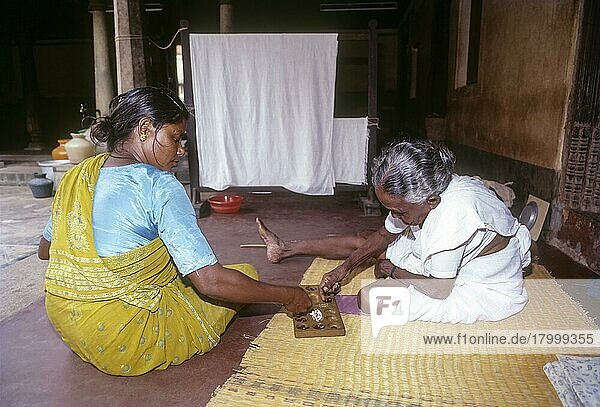 Zwei Frauen sitzen auf dem Boden und spielen Pallanguzhi in Chettinad  Tamil Nadu  Indien. Pallanguzhi wurde hauptsächlich von tamilischen Frauen als Zeitvertreib gespielt. Pallanguzhi ist ein städtisches Brettspiel. Die Bretter gibt es in verschiedenen Formen und Größen  aber grundsätzlich haben sie sieben Gruben auf jeder Seite und die beiden Spieler sitzen sich gegenüber