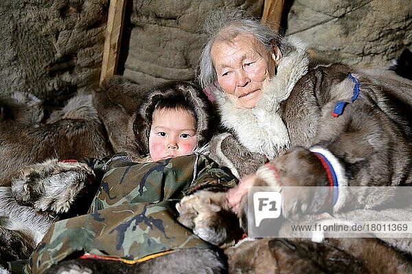 Eine ältere Frau der Nenzen mit ihrem Enkel. Beide sind in ihre Wintermäntel aus Rentierfell gekleidet und sitzen in ihrem Zelt  Chum  Distrikt Yar-Sale  Jamal  Nordwest-Sibirien  Russland  Europa