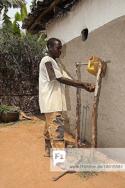 Mann wäscht Hände unter selbstgebautem Wasserhahn aus Kunststoffbehälter  Ruanda  Afrika