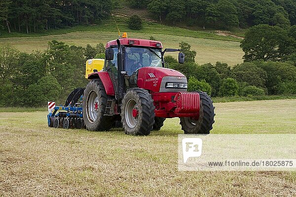 Lohnunternehmer mit McCormick MC120 Traktor und ERTH Agriseeder Präzisionsschlitz-Sämaschine  sät Kleesamen auf dem Feld eines Biobetriebs aus  Powys  Wales  Juni
