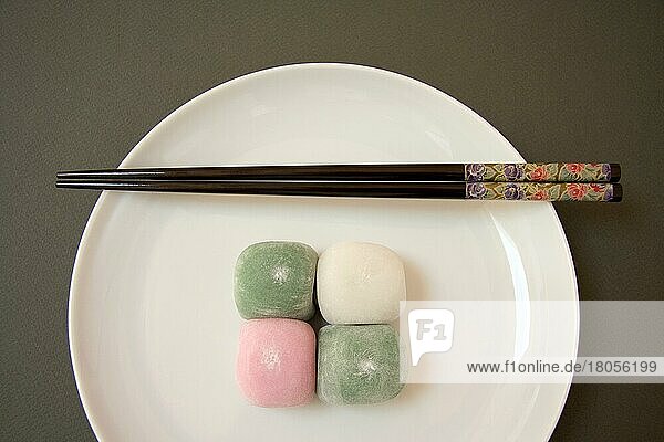 Vier japanische Mochi-Bonbons mit Essstäbchen auf einem Porzellanteller