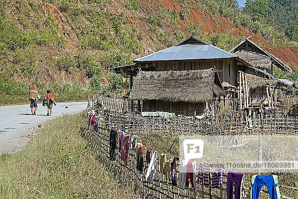 Ein burmesischer Mann trägt Feuerholz auf seinem Rücken und Wäsche  die in der Sonne am Zaun entlang der Straße in einem ländlichen Dorf im Tachileik District  Shan State  Myanmar  trocknet  Asien