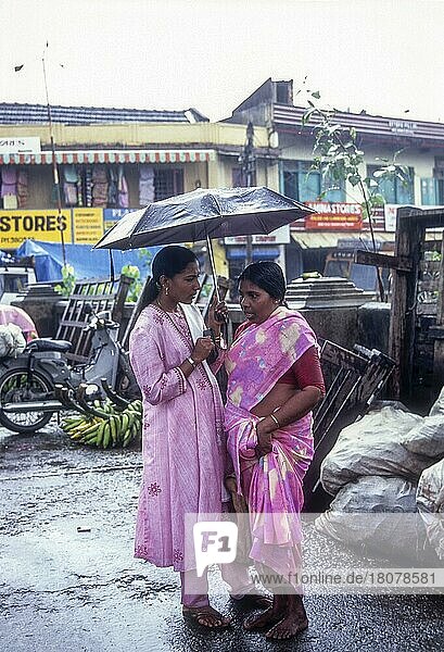 Mother and daughter under umbrella during rainy monsoon season at Ernakulam kochi Cochin  Kerala  India  Asia