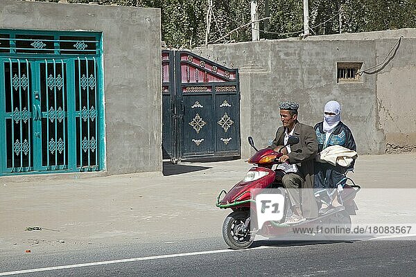 Uigurischer Mann in traditioneller muslimischer Kleidung  Kind und Frau mit islamischem Schleier fahren auf einem Motorroller  Xinjiang  China  Asien