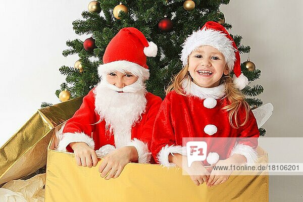 Kinder verkleidet als Weihnachtsmann  in großem Geschenk  am Weihnachtsbaum  geschmückter Weihnachtsbaum  Weihnachtsmänner  Weihnachtsgeschenk  Nikolaus  Nikolauskostüm  Kiste