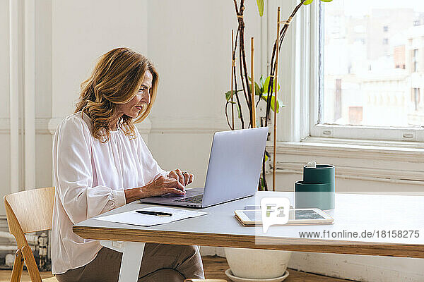 Reife Geschäftsfrau arbeitet am Laptop am Schreibtisch im Bürostudio