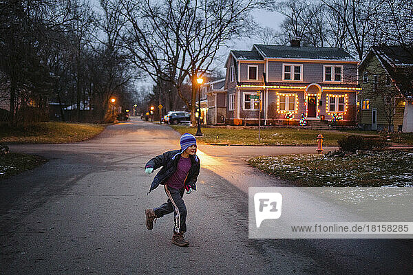 Ein Junge in Winterkleidung spielt in der Abenddämmerung auf einer beleuchteten Straße