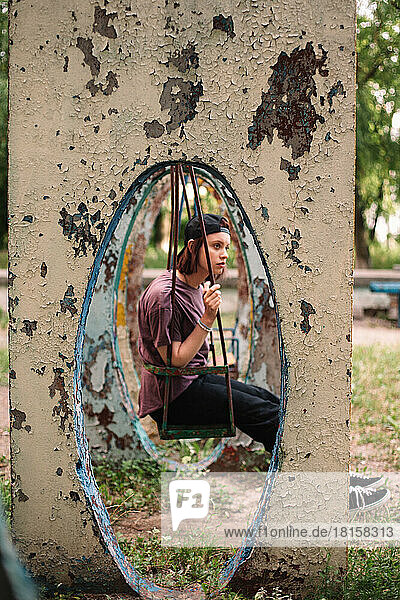 Junge Punkerin sitzt auf einer Schaukel auf einem verlassenen Spielplatz im Sommer