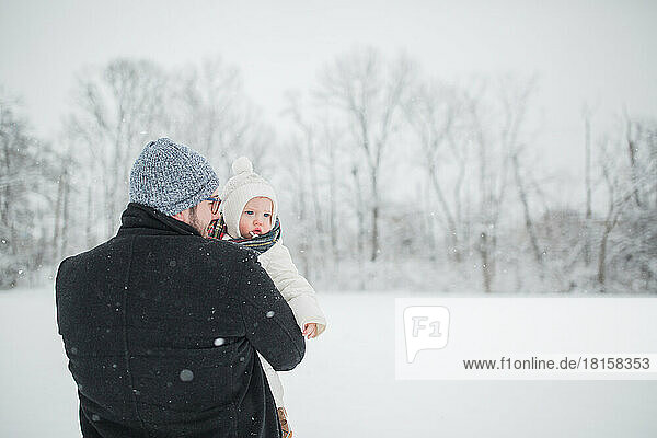 30-year-old Caucasian father holds baby boy in snowy field.