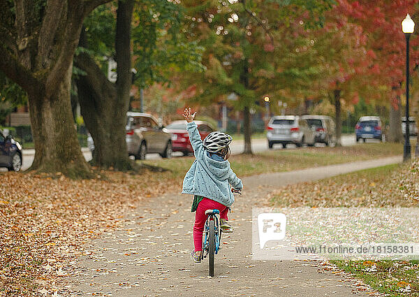 A proud little girl bikes one-handed down a city park path