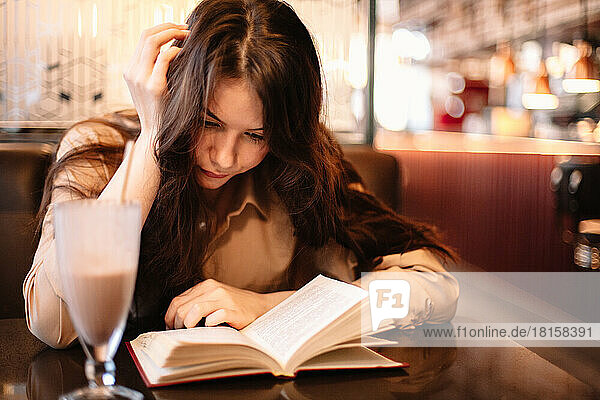 Young woman reading book while sitting in cafe