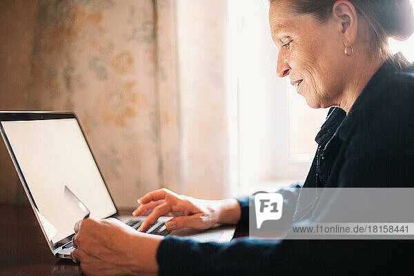 Happy mature woman using laptop computer and credit card at home