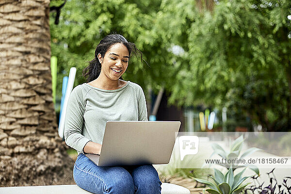 Lächelnde Freiberuflerin  die einen Laptop benutzt und auf einer Bank sitzt