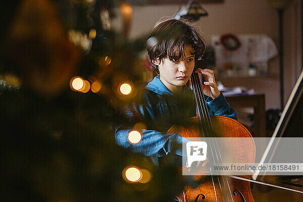 Ein ernstes Kind spielt Cello im Licht des Weihnachtsbaums