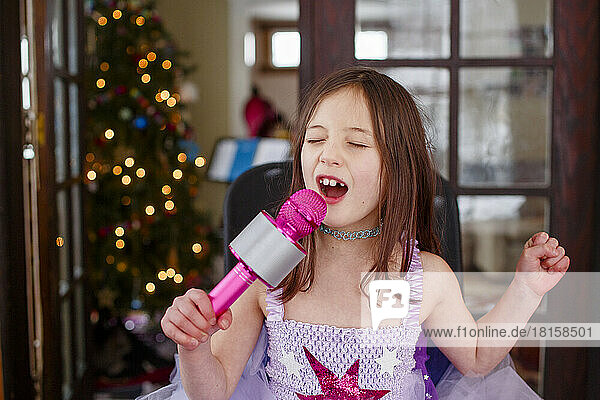 ein kleines Mädchen im Kostüm singt zu Hause laut in ein Mikrofon