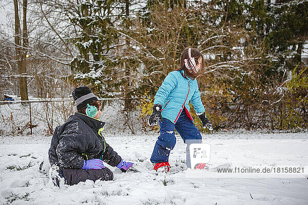 Ein Junge bringt seiner kleinen Schwester im Winter das Snowboardfahren bei