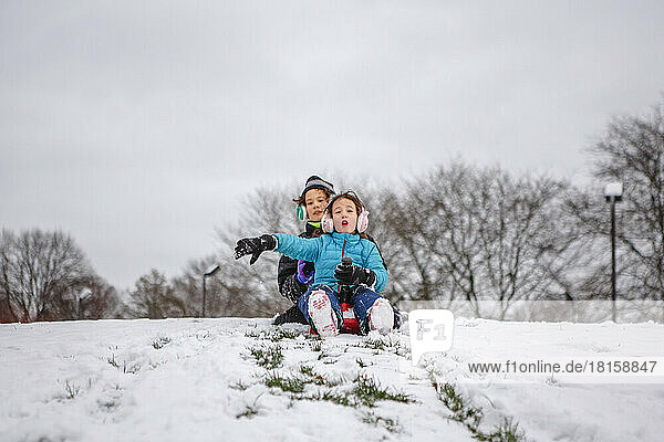 Two children slide down a snowy hill together in winter