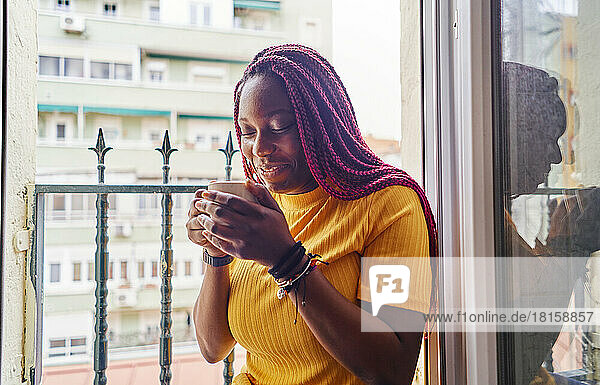 junge afrikanisch-amerikanische Frau trinkt Kaffee am Küchenfenster sitzend