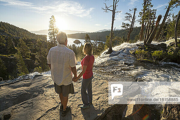 A man and a woman hold hands at the top of Eagle Falls at sunrise.