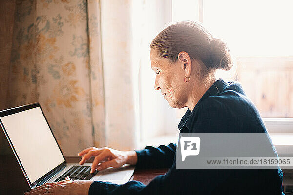 Glückliche reife Frau  die einen Laptop bei der Arbeit zu Hause benutzt