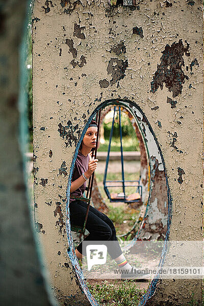 Junge Punkerin sitzt auf einer Schaukel auf einem verlassenen Spielplatz im Sommer