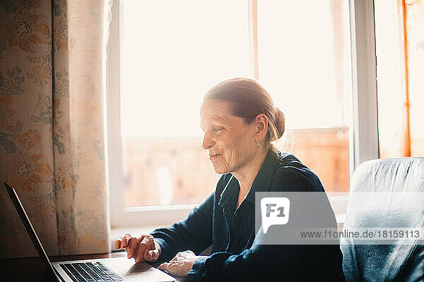 Glückliche lächelnde reife Frau  die einen Laptop bei der Arbeit zu Hause benutzt